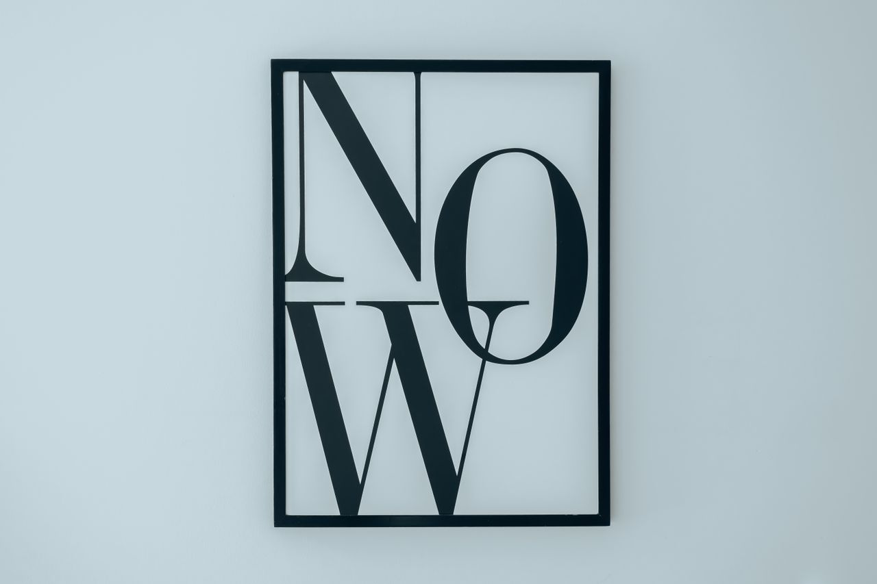 Cadre noir épuré avec le mot NOW sur fond blanc, illustrant une décoration minimaliste.